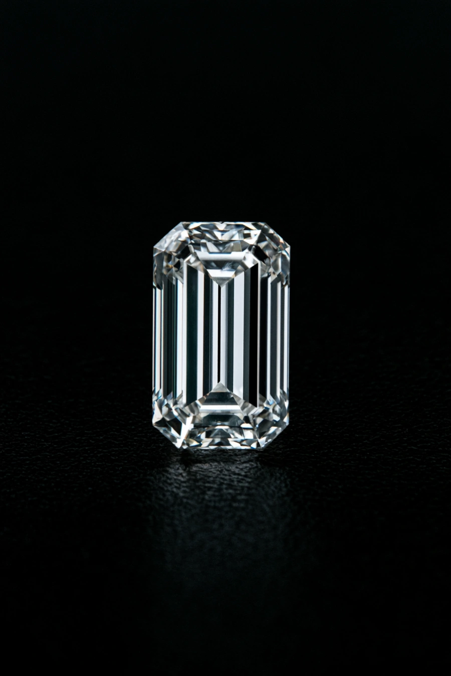 Baguette-cut diamond with a slim rectangular shape, cropped corners, and sleek step facets standing upright on black surface