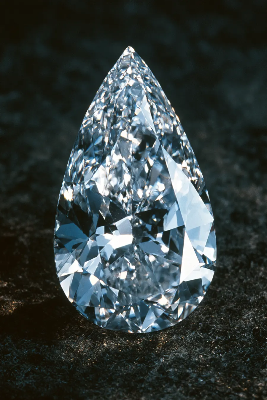 Pear-cut diamond standing upright with a pointed tip, rounded base, and brilliant facets sparkling on a dark textured surface