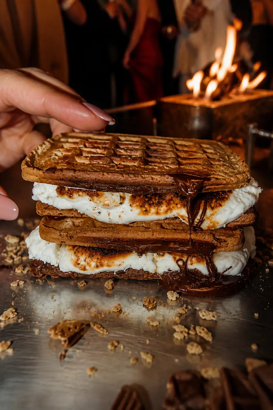 Hand lifting a chocolate waffle from stacked s’mores filled with toasted marshmallow and dripping melted chocolate