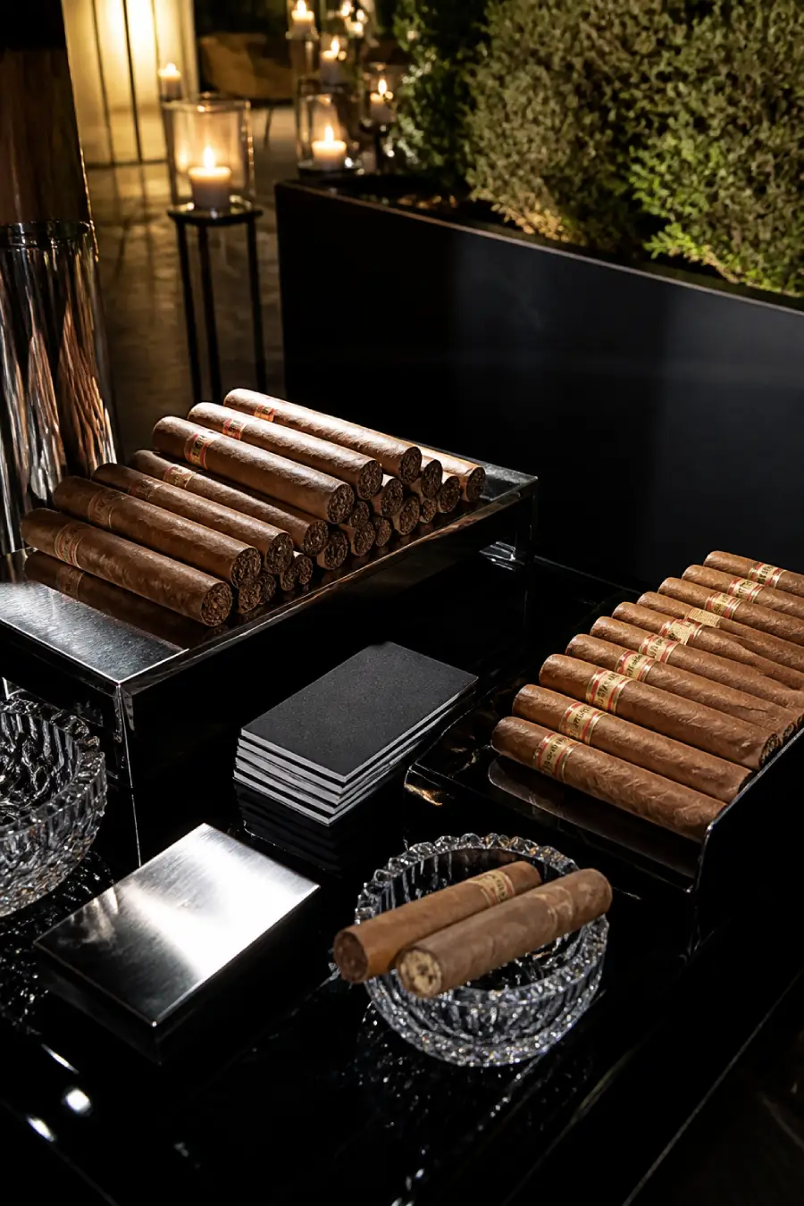 Rows of premium cigars rest on black lacquer trays with crystal ashtrays and candles at an elegant wedding cigar bar at dusk.