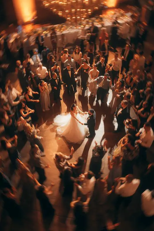 Bride and groom share a romantic first dance surrounded by guests in a glowing circle under warm chandelier light. Bride and groom share a romantic first dance surrounded by guests in a glowing circle under warm chandelier light.