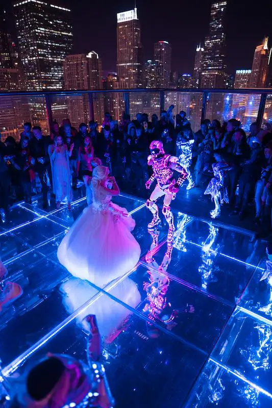 Bride dancing with LED robot performer on a glowing rooftop dance floor overlooking a city skyline at night. Bride dancing with LED robot performer on a glowing rooftop dance floor overlooking a city skyline at night.