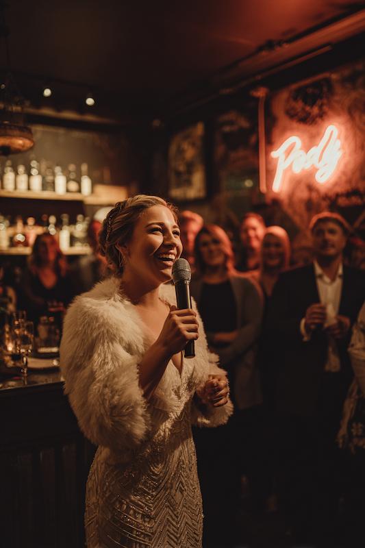 Bridesmaid in a beaded gown with a fur wrap giving a joyful toast at a warmly lit wedding reception bar. Bride in a beaded gown with a fur wrap giving a joyful toast at a warmly lit wedding reception bar.