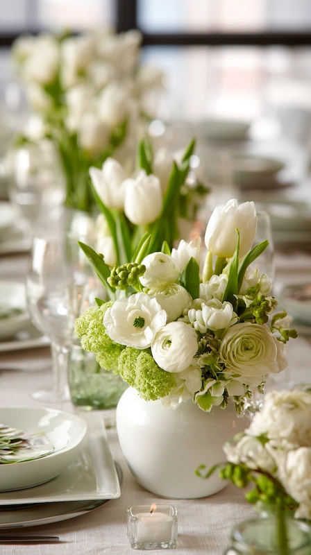 All white wedding table with tulips and ranunculus in bud vases, soft greenery accents, candlelight, and clean modern place settings