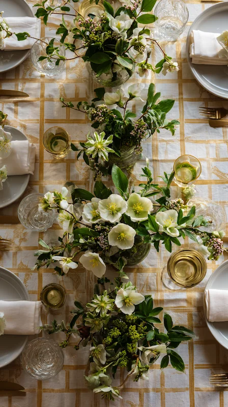 Overhead wedding table with white florals and greenery centerpieces, gold grid linen, layered plates, glassware, and refined styling