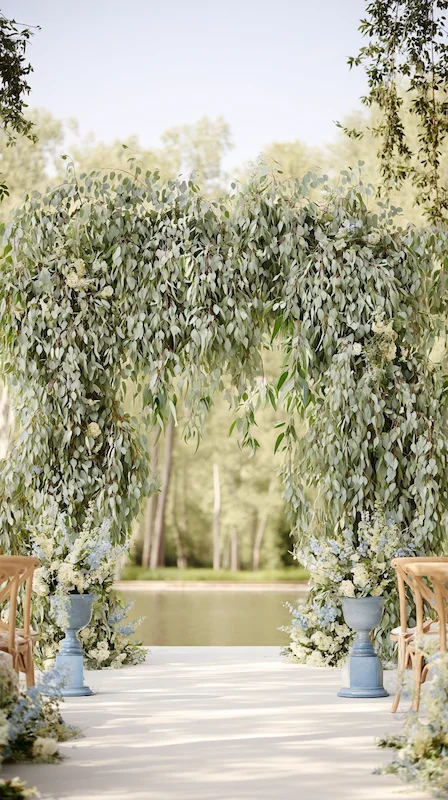 39 Wedding Arch Ideas That Will Make Your Ceremony Unforgettabl 10 Eucalyptus wedding arch with cascading greenery and soft florals set beside a serene lakeside outdoor ceremony backdrop