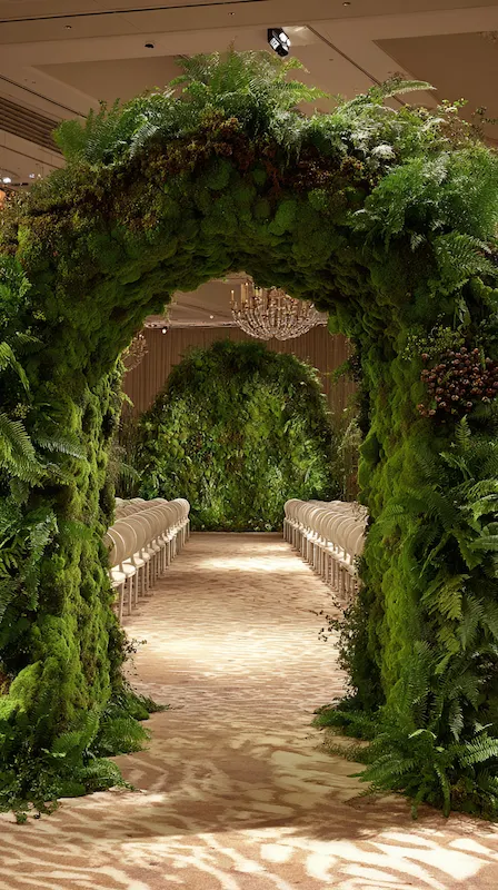 39 Wedding Arch Ideas That Will Make Your Ceremony Unforgettabl 14 Luxury wedding ceremony aisle beneath towering moss and fern arch tunnel with white chairs leading to lush floral backdrop