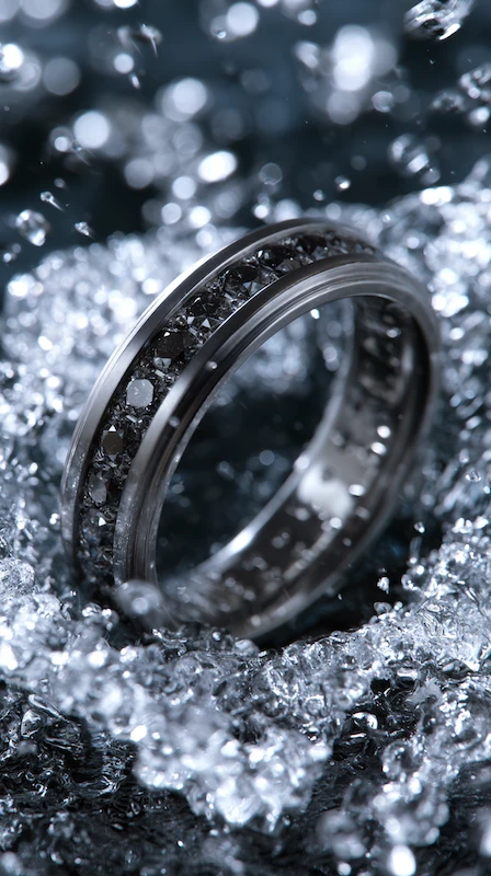 Channel-set black diamond wedding band surrounded by sparkling ice crystals in a dramatic luxury close-up scene