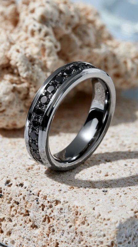 Black diamond channel-set men’s wedding band in polished black metal resting on textured stone in soft natural light