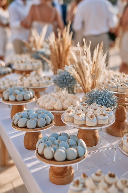 Dusty blue wedding dessert table with macarons, mini desserts, dried pampas grass, and elegant outdoor reception styling.