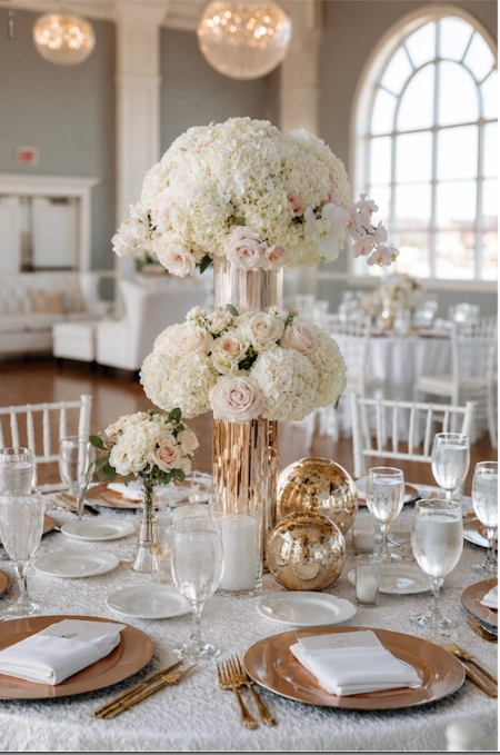 Why Weddings Go Over Budget (And Exactly Where the Money Goes) 4 Elegant wedding reception table with tall white floral centerpieces, gold accents, and formal place settings.