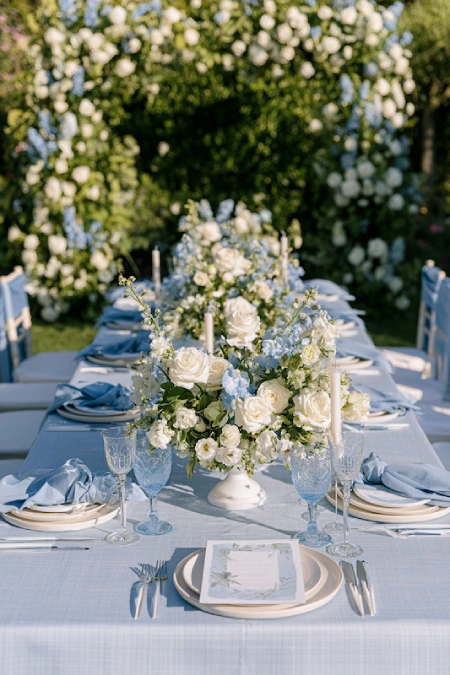 Garden wedding reception with dusty blue and ivory floral centerpieces, soft blue linens, and romantic outdoor tablescape.