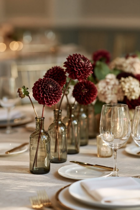 25 Fall Wedding Centerpieces With Main Character Energy (Cozy, Never Costume-y) 20 Burgundy dahlia bud vases create a simple, elegant wedding centerpiece with candlelight on a round reception table
