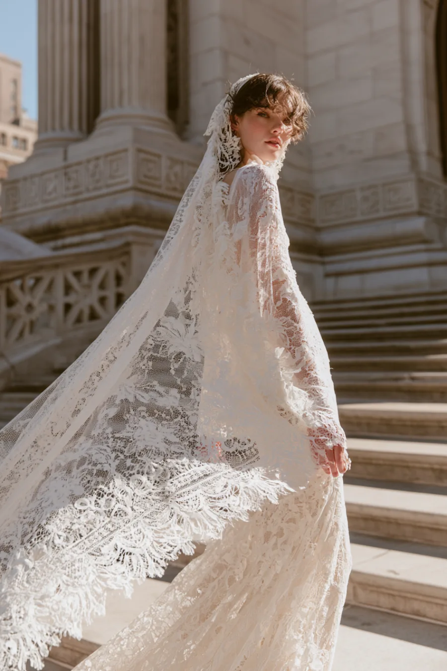 Bride in a Chantilly lace wedding dress with matching lace veil flowing across grand stone steps in elegant outdoor portrait