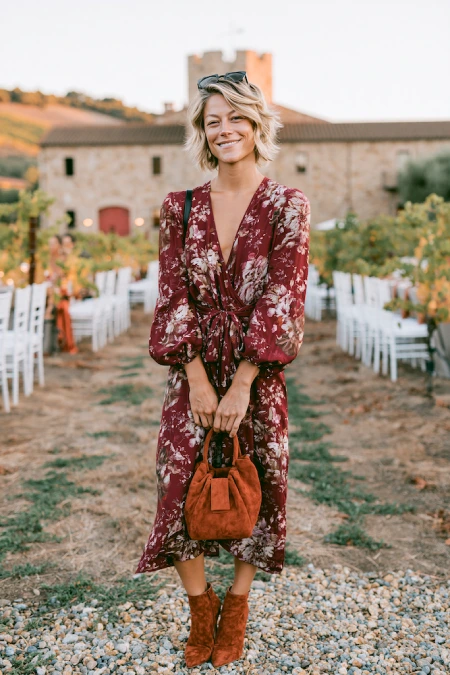 The Perfect Rehearsal Dinner Dress for Guests: Your Complete Outfit Guide 16 Woman in a burgundy floral midi dress and suede boots at a vineyard rehearsal dinner with rustic fall style