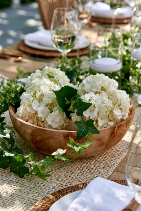 Garden party rehearsal dinner centerpiece with white hydrangeas in a wooden bowl and trailing ivy accents