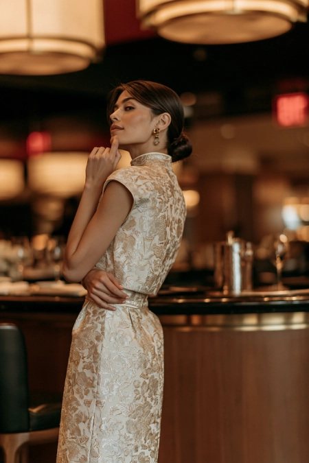 Rehearsal Dinner Dresses for the Bride: What to Wear at Every Formality Level 13 Bride-to-be in a gold brocade high neck dress with cap sleeves and sleek bun posing in an upscale rehearsal dinner restaurant