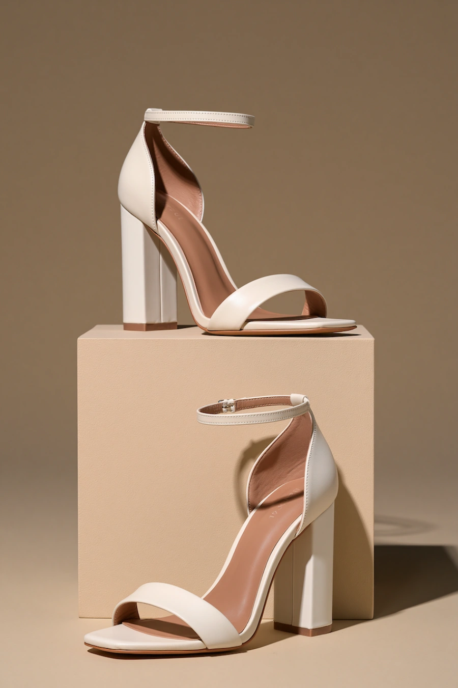 Wedding Shoes for the Bride: 27 Beautiful Ideas That Balance Style and Comfort 9 Ivory block heel bridal sandals with ankle straps and open toes displayed on pedestal blocks in a minimalist studio setting