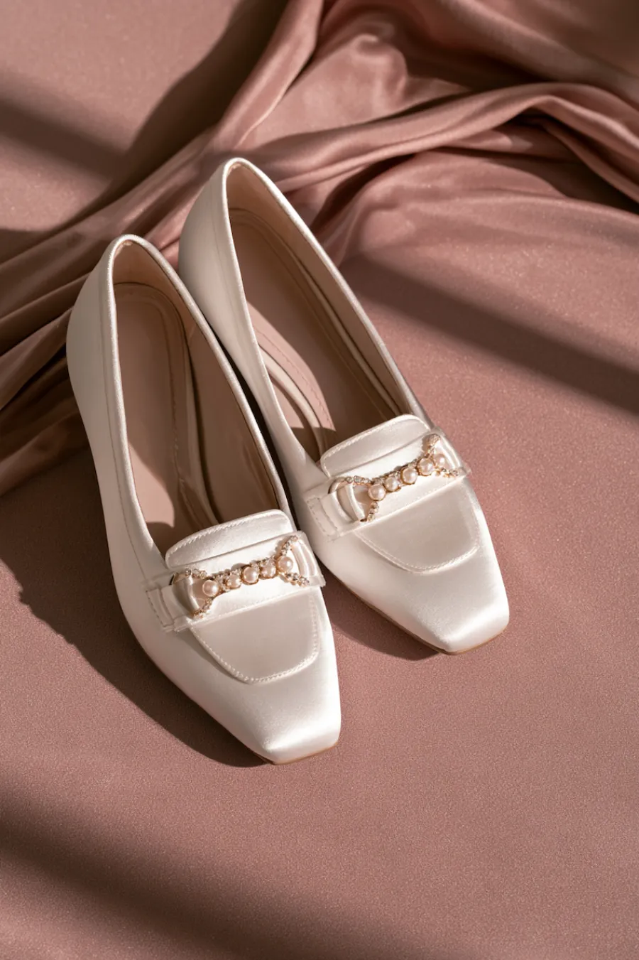 Wedding Shoes for the Bride: 27 Beautiful Ideas That Balance Style and Comfort 18 Ivory satin bridal flats with square toes and pearl chain embellishments displayed on blush fabric for elegant wedding style
