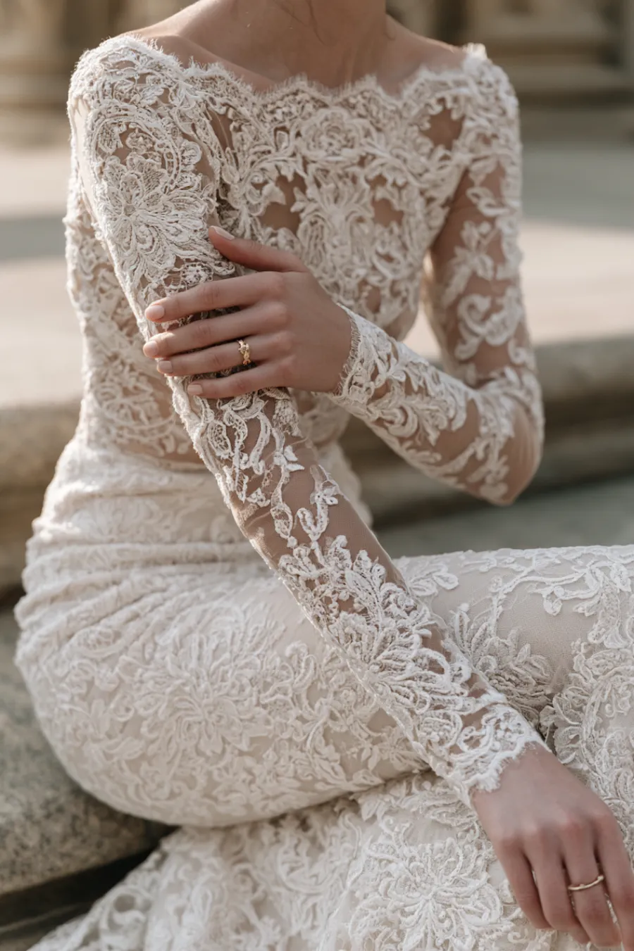Bride wearing a fitted lace wedding dress with illusion long sleeves and floral embroidery, highlighting intricate bridal details