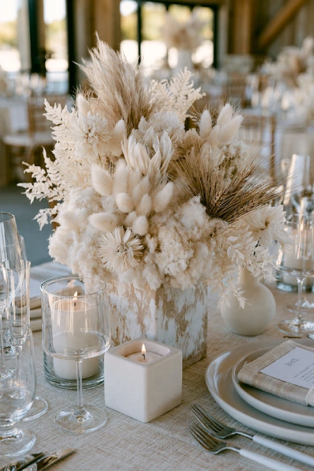 25 Fall Wedding Centerpieces With Main Character Energy (Cozy, Never Costume-y) 14 Neutral dried floral centerpiece with pampas grass, bunny tails, and candles on an elegant rustic wedding reception table