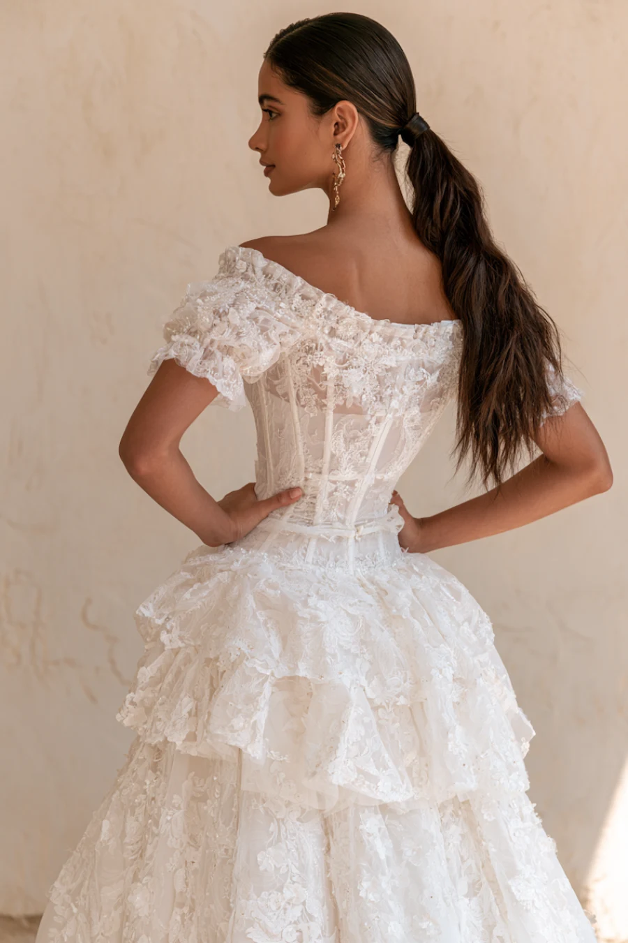 Bride wearing an off-the-shoulder lace corset wedding dress with layered ruffles and floral appliqué viewed from the back