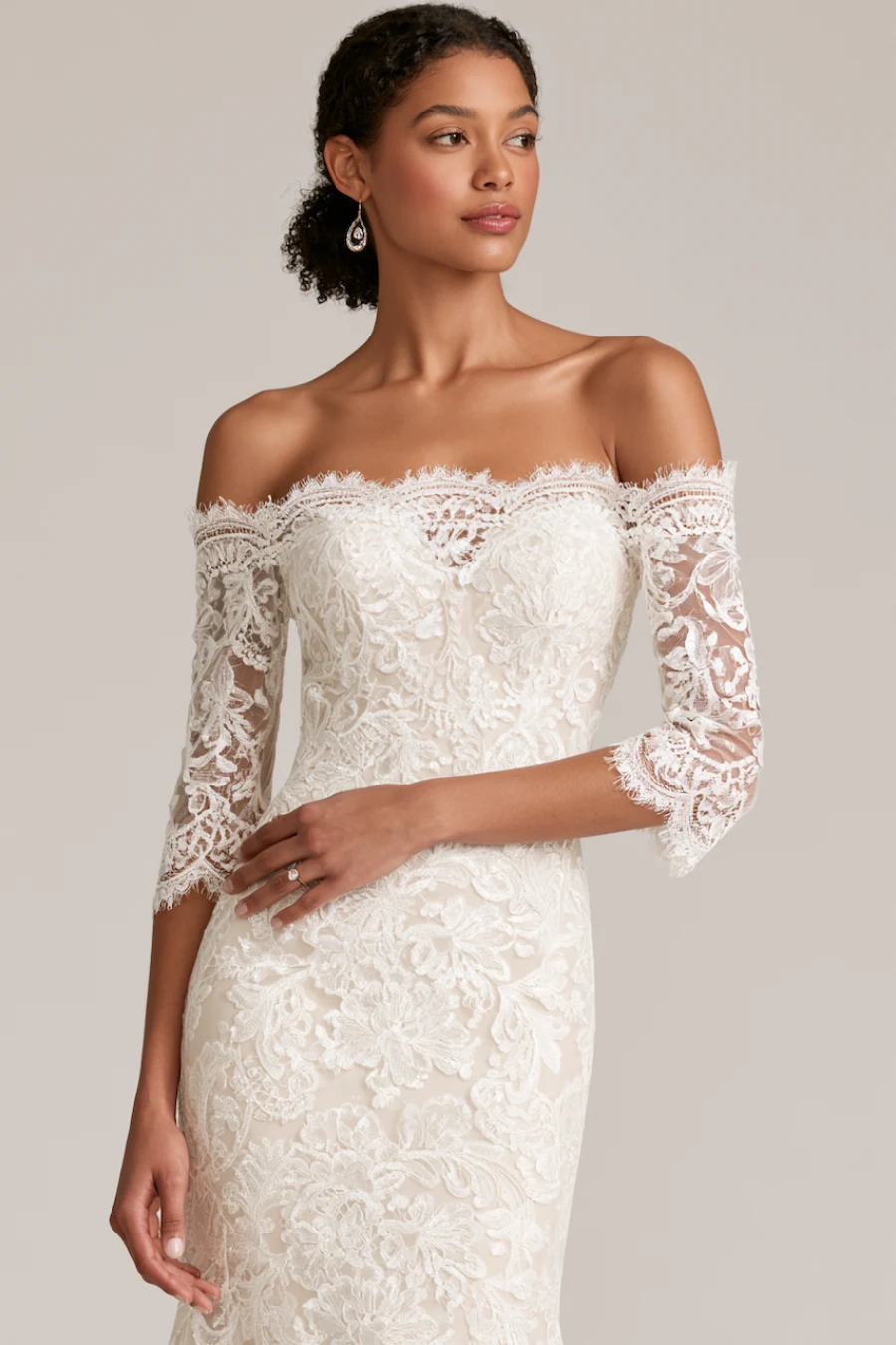 Bride wearing an off-the-shoulder lace wedding dress with illusion sleeves, floral embroidery, and fitted bridal silhouette