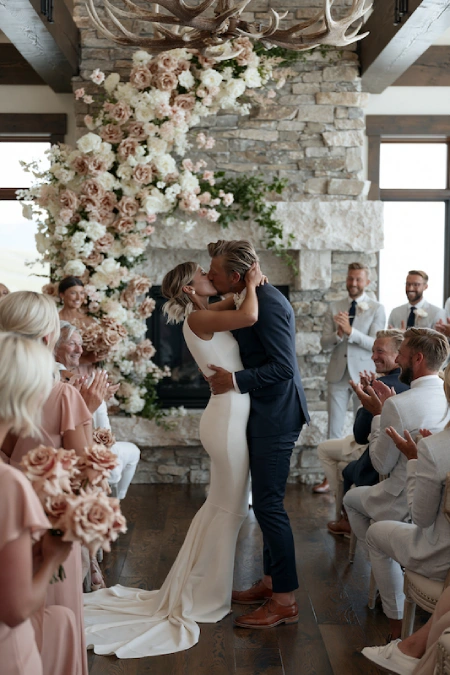 Sage Green and Terracotta Wedding: The Earthy Duo That Understood the Assignment 6 Bride and groom share their first kiss beneath a blush floral ceremony arch in a rustic stone venue surrounded by applauding guests
