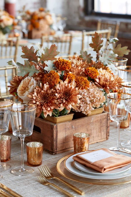 25 Fall Wedding Centerpieces With Main Character Energy (Cozy, Never Costume-y) 4 Rustic wooden box centerpiece with bronze mums, marigolds, hydrangeas, and autumn leaves on an elegant fall wedding table
