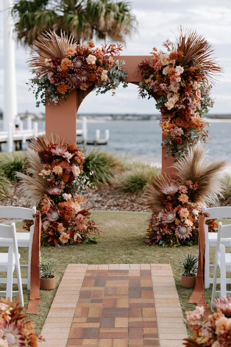 Terracotta Wedding Color Scheme: The Coziest, Most Iconic Palette Around 14 Terracotta wedding ceremony arch with pampas grass, dried florals, and waterfront coastal wedding backdrop