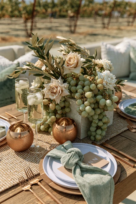 25 Fall Wedding Centerpieces With Main Character Energy (Cozy, Never Costume-y) 15 Vineyard wedding centerpiece with ivory roses, cascading green grapes, olive branches, and candlelight on an outdoor table