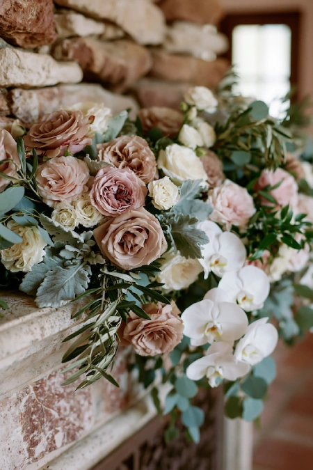Sage Green and Terracotta Wedding: The Earthy Duo That Understood the Assignment 2 Wedding fireplace mantel with blush roses, white orchids, eucalyptus, and lush greenery in a rustic stone reception venue