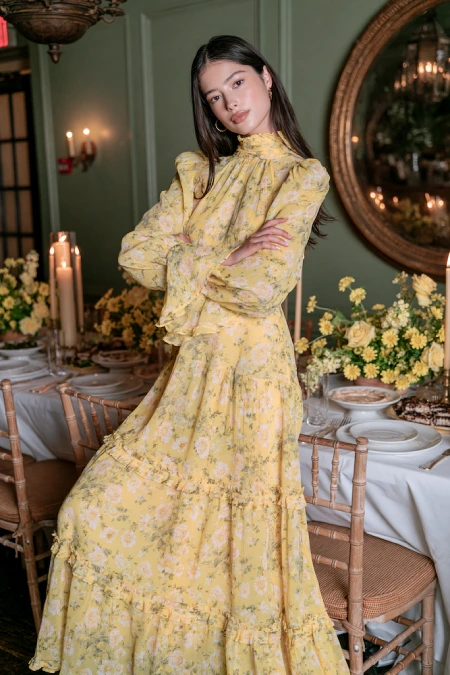 Rehearsal Dinner Dresses for the Bride: What to Wear at Every Formality Level 16 Bride-to-be in a yellow floral chiffon maxi dress with high neck and ruffles at a candlelit rehearsal dinner with yellow roses