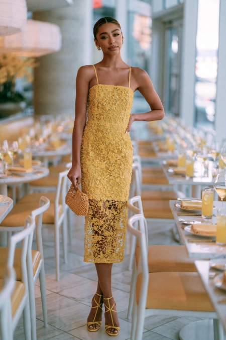 Rehearsal Dinner Dresses for the Bride: What to Wear at Every Formality Level 11 Bride-to-be in a yellow lace midi dress with sheer hem and matching heels standing in a bright modern rehearsal dinner venue