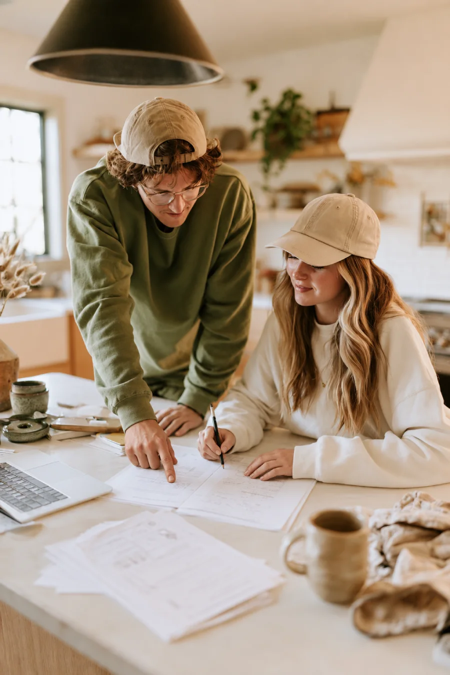 Gen Z couple reviewing wedding planning documents together at a kitchen table, with a laptop, notes and a pencil in view